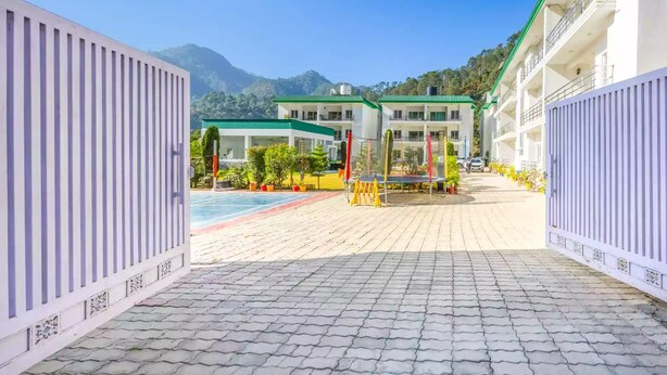 A hotel entrance with a paved pathway leading to a pool area, surrounded by greenery and mountains in the background. - Alaya Stays By Elivaas Kingdom Heartz (Nainital)