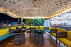 An outdoor seating area with yellow cushions and wicker furniture, under a patterned canopy. - Alaya Stays By Elivaas Kingdom Heartz (Nainital)