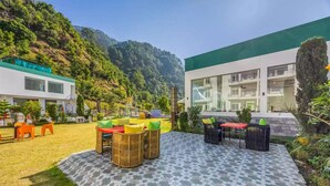 A courtyard with outdoor seating, a patterned tile floor, and a view of a mountain. - Alaya Stays By Elivaas Kingdom Heartz (Nainital)