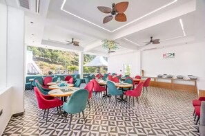 Un restaurante con una decoración moderna, que presenta un suelo con estampado geométrico, sillas coloridas y ventiladores de techo.