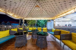 An outdoor seating area with yellow cushions and wicker furniture, under a patterned canopy. - Alaya Stays By Elivaas Kingdom Heartz (Nainital)