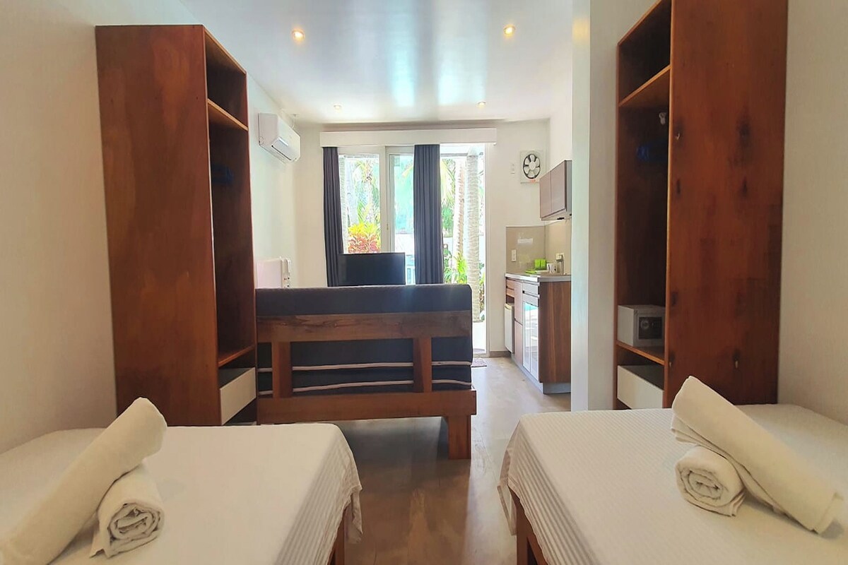 Ein Hotelzimmer mit zwei Betten, einer hölzernen Sitzbank, einer Küchenzeile und Blick ins Freie.