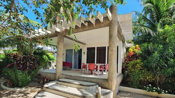 A covered outdoor seating area with steps leading up to a patio, surrounded by lush greenery and palm trees. - Pili Beach Resort Agmanic By Zuzu (Santa Fe)