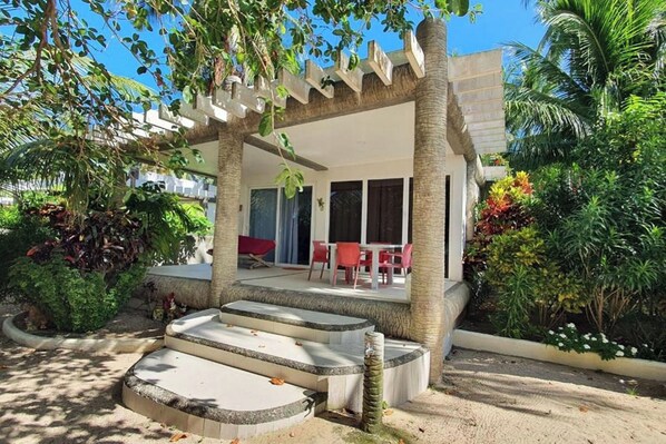 A covered outdoor seating area with steps leading up to a patio, surrounded by lush greenery and palm trees. - Pili Beach Resort Agmanic By Zuzu (Santa Fe)