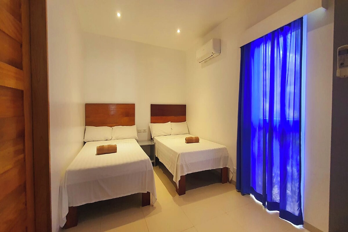 A hotel room with two single beds, a wooden headboard, white bedding, and a blue curtain.
