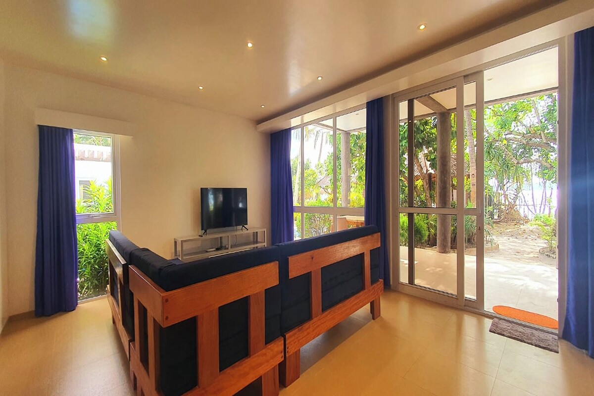 A room with a wooden bench, a television, and large windows with curtains.