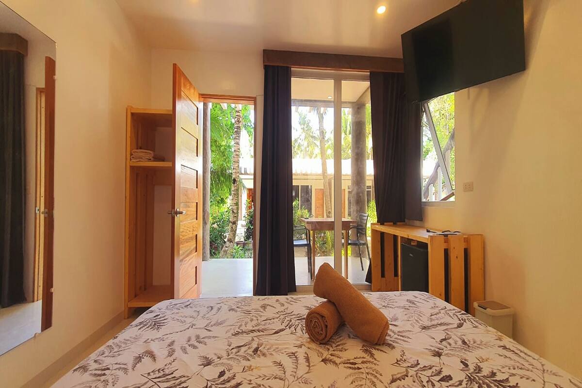Une chambre à coucher comprenant un lit, une télévision, une armoire et une porte-fenêtre coulissante donnant sur un balcon.