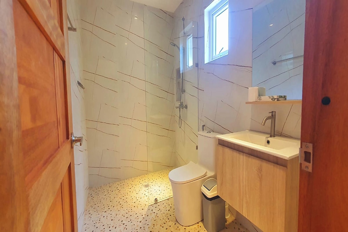 A bathroom with a shower, toilet, sink, and wooden cabinets.