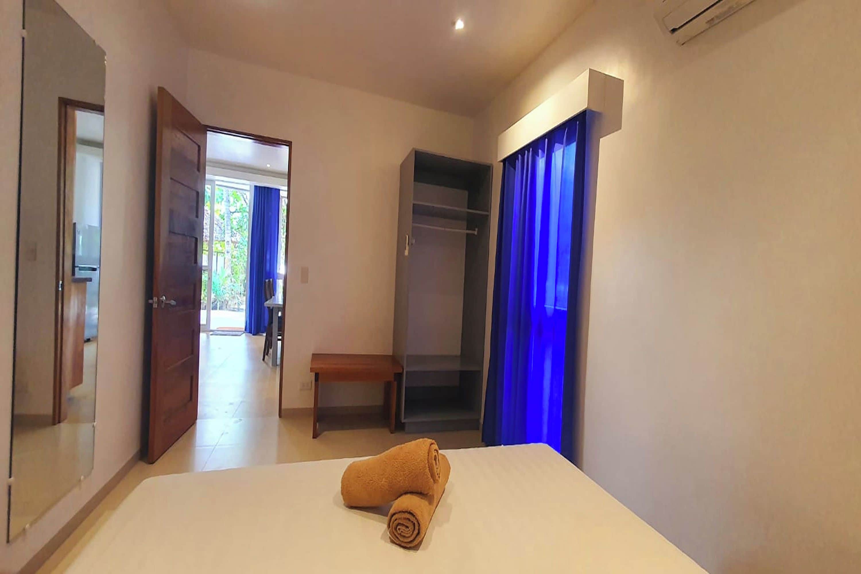 Habitación de hotel con cama, armario, banco y puerta que da a un balcón.