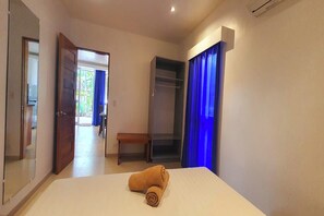 Een hotelkamer met een bed, een kledingkast, een bankje en een deur naar een balkon.