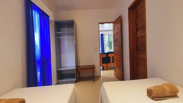 A hotel room with two beds, a wardrobe, a bench, and a view of the outside.