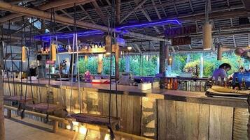 Una zona de bar con un mostrador de madera rústica, luces colgantes y vistas a la vegetación exterior.