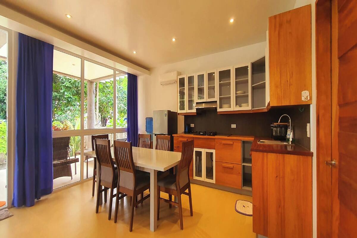 Une cuisine moderne avec des meubles en bois, une table à manger avec des chaises et de grandes fenêtres ornées de rideaux bleus.