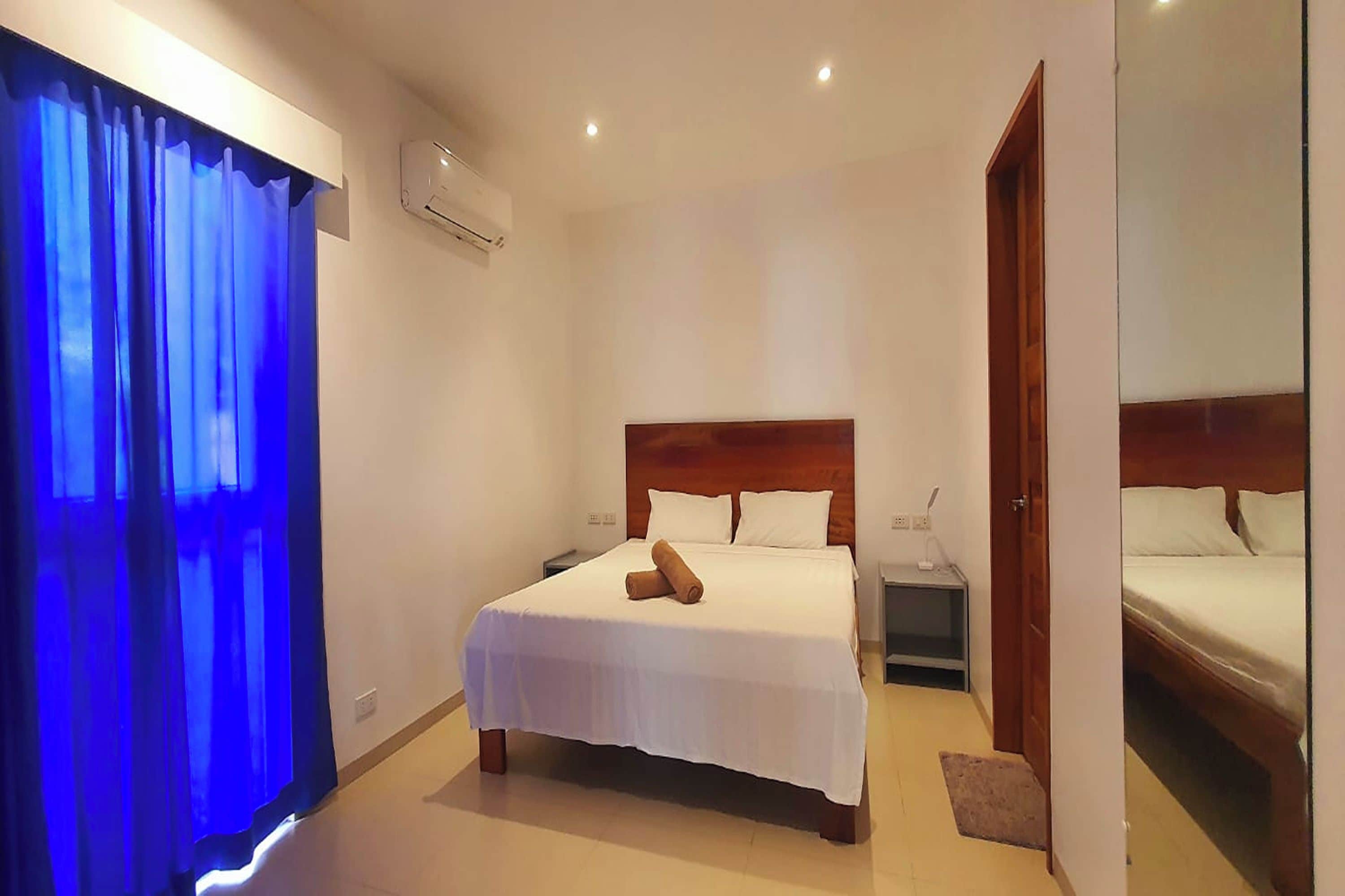 A hotel room with a large bed, a nightstand, a wooden headboard, and a mirror on the wall.