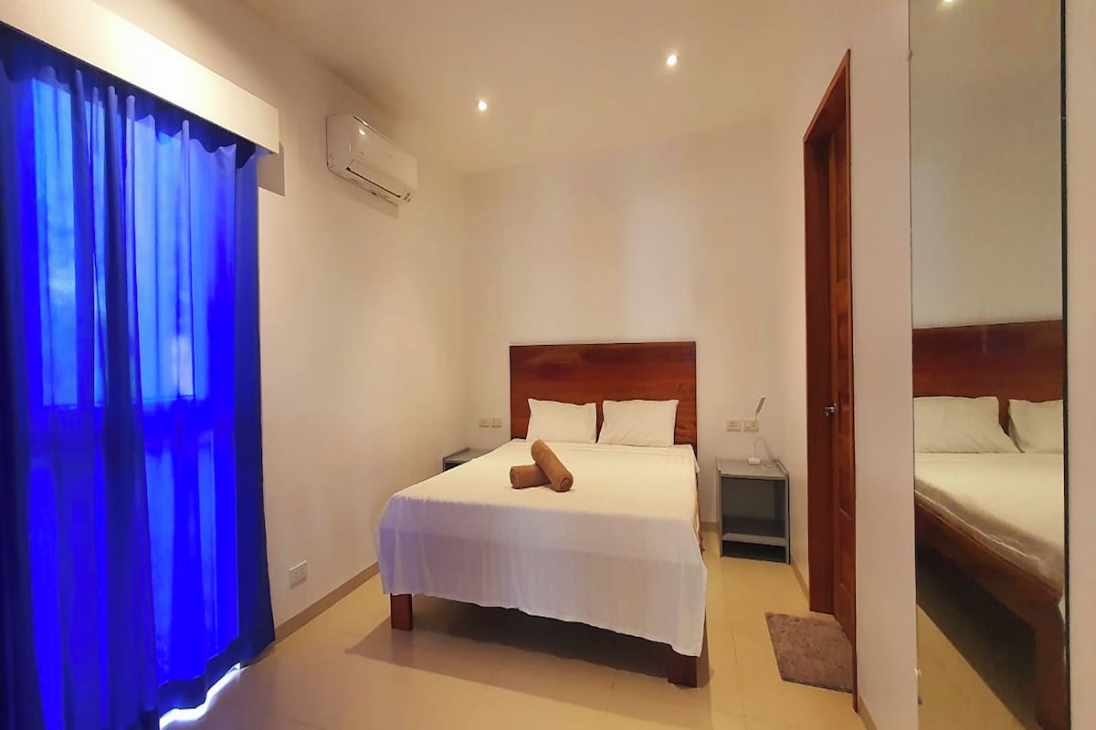 A hotel room with a large bed, a nightstand, a wooden headboard, and a mirror on the wall.