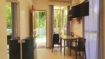 A compact hotel room with a kitchenette, a dining area, and a TV mounted on the wall.