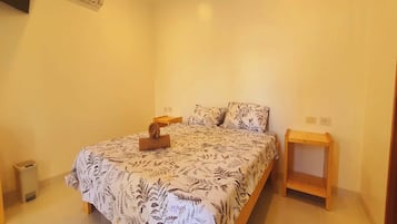 A bedroom with a bed, a bedside table, a wooden nightstand, and a wall-mounted air conditioner.