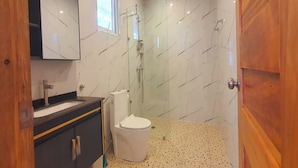 Casa de banho com sanita branca, lavatório e cabine de duche com vidro.
