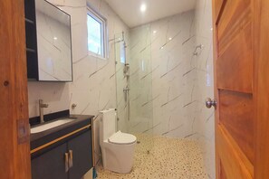 A bathroom with a white toilet, a sink, and a glass-enclosed shower. - Pili Beach Resort Agmanic By Zuzu (Santa Fe)