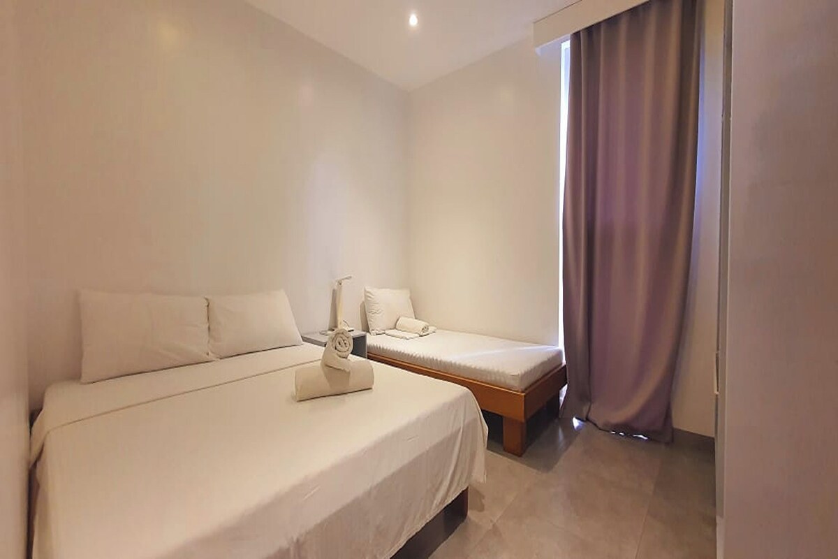 A hotel room with two single beds, a nightstand, and a window with curtains.