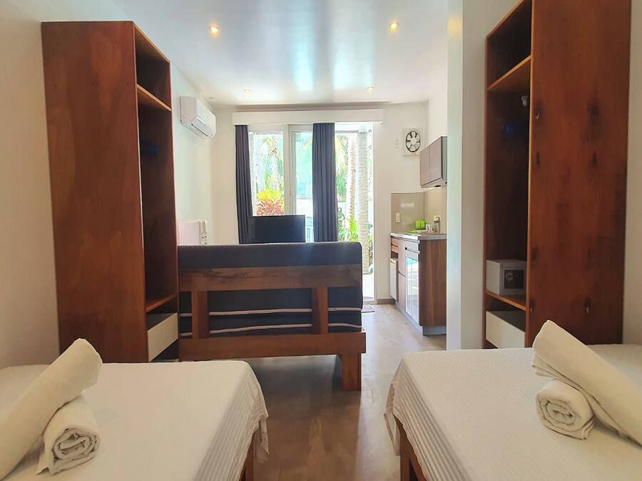 Habitación de hotel con dos camas, un banco de madera, kitchenette y vistas al exterior.