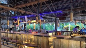 A bar area with a rustic wooden counter, hanging lights, and a view of greenery outside. - Pili Beach Resort Agmanic By Zuzu (Santa Fe)