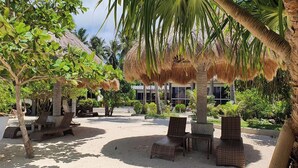 A beachside lounge area with thatched-roof structures, lounge chairs, and a sandy ground. - Pili Beach Resort Agmanic By Zuzu (Santa Fe)