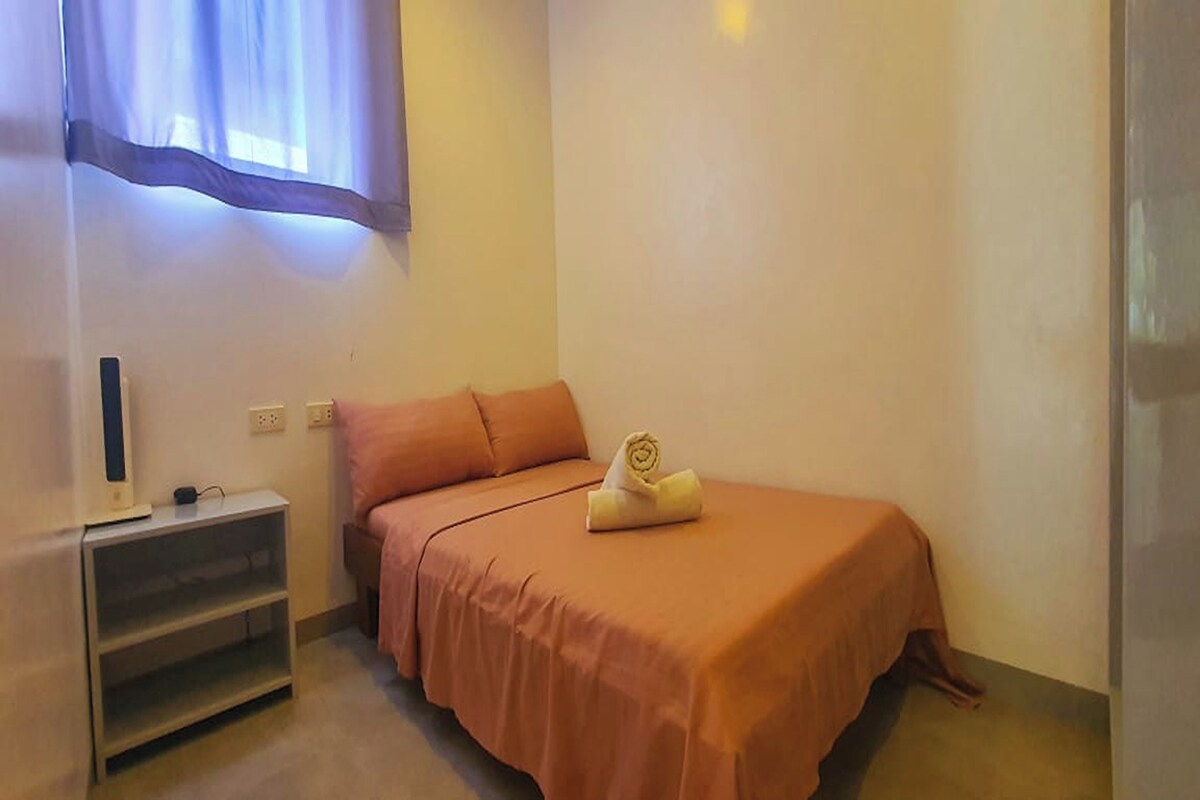 Ein kleines Zimmer mit einem Einzelbett, einem Nachttisch und einem Fernseher.