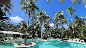 Área de piscina com palmeiras e céu azul e límpido.