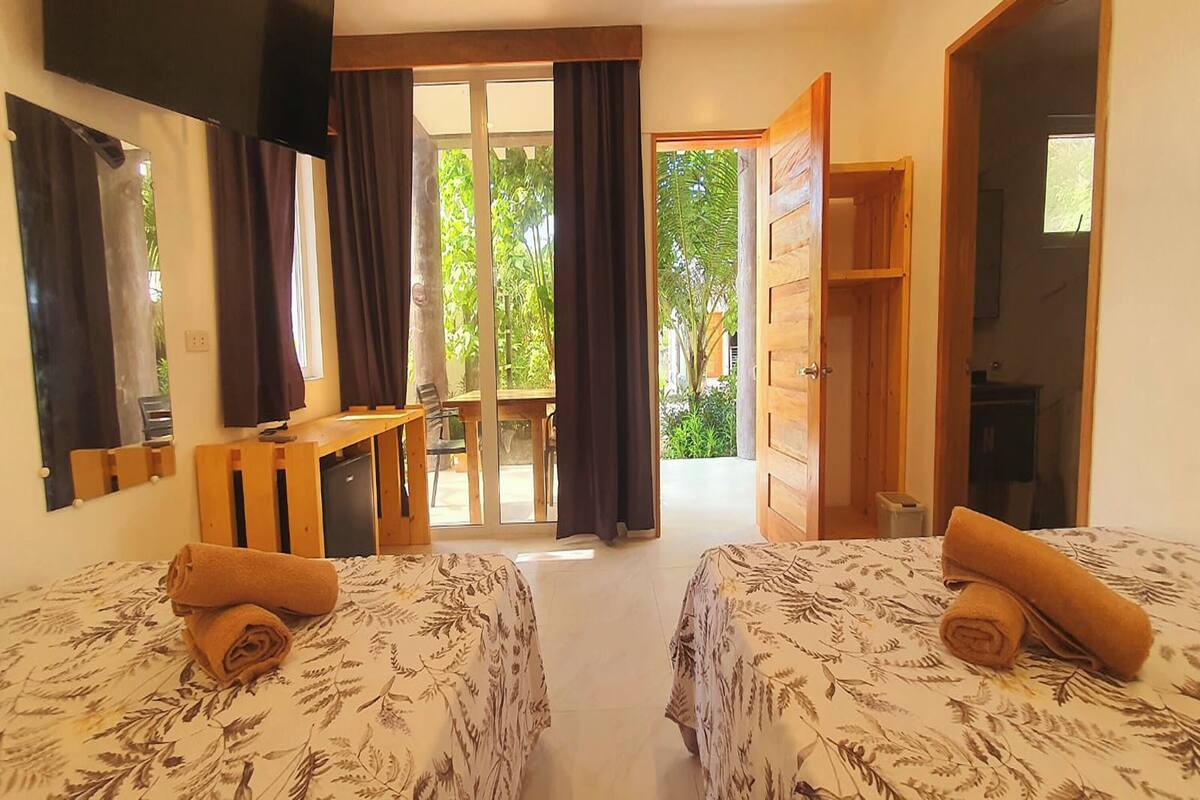 Une chambre avec deux lits, un bureau et une vue sur la verdure.