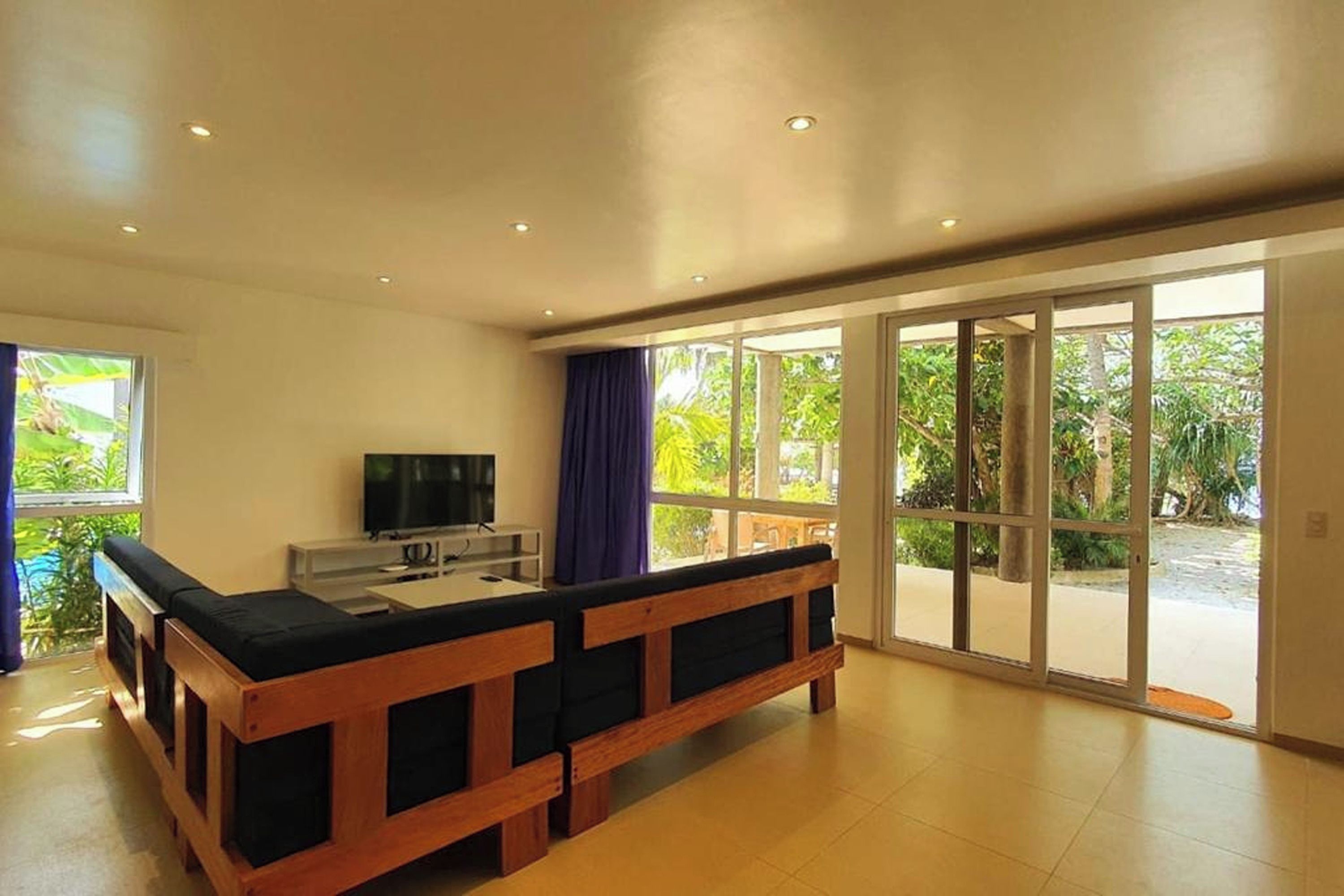 A spacious room with a large wooden bench, a television, and a sliding glass door leading to a garden.