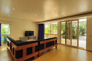 Ein geräumiges Zimmer mit einer großen Holzlounge, einem Fernseher und einer Glastür, die in einen Garten führt.