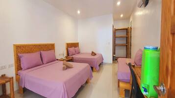 Habitación de hotel con dos camas, cabecera de madera, una mesita pequeña y dispensador de agua verde.