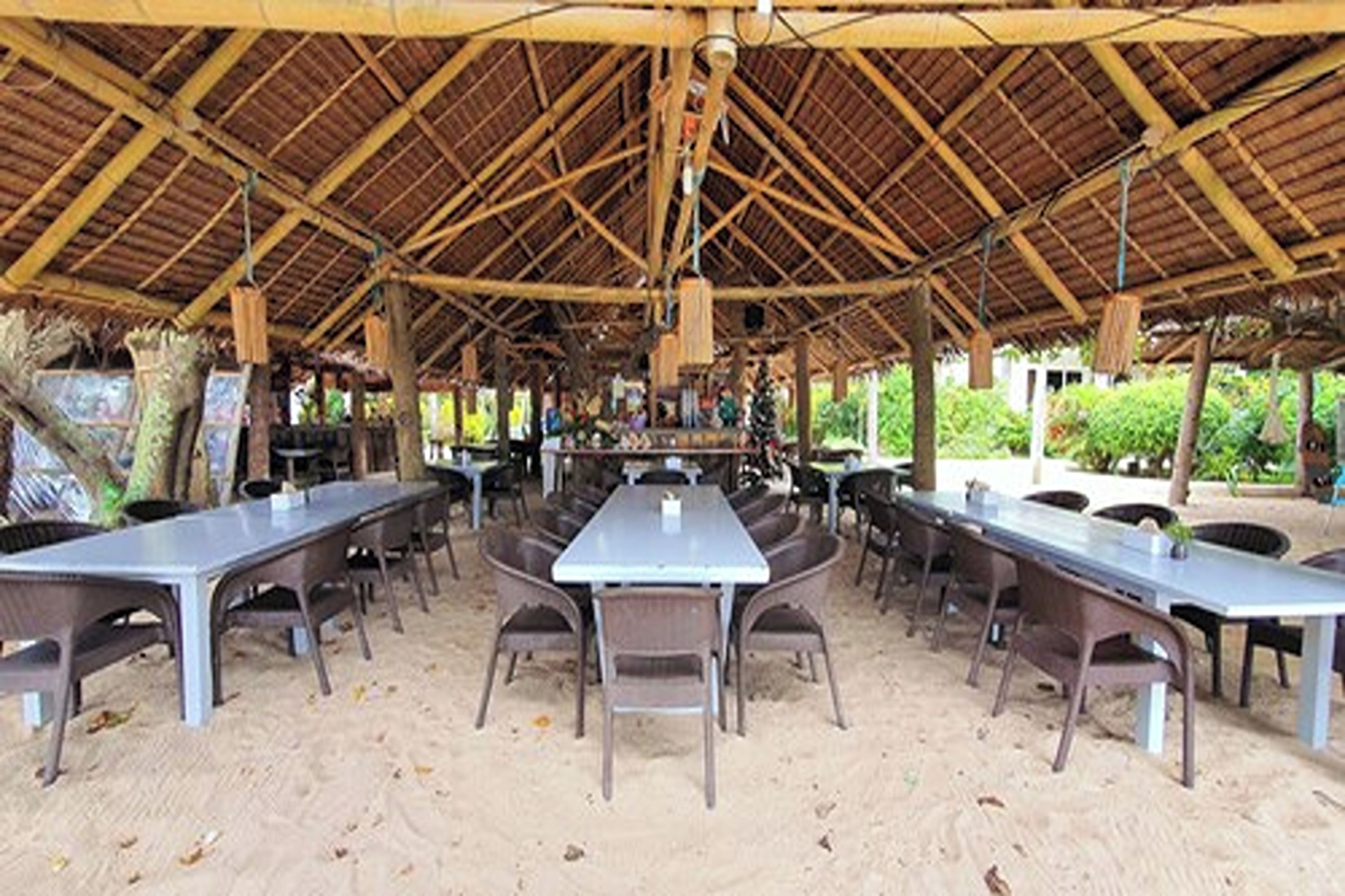An outdoor dining area with multiple tables and chairs under a thatched roof.