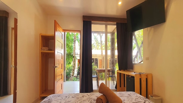 Quarto com cama, televisão, guarda-roupa e porta de vidro deslizante para uma varanda.