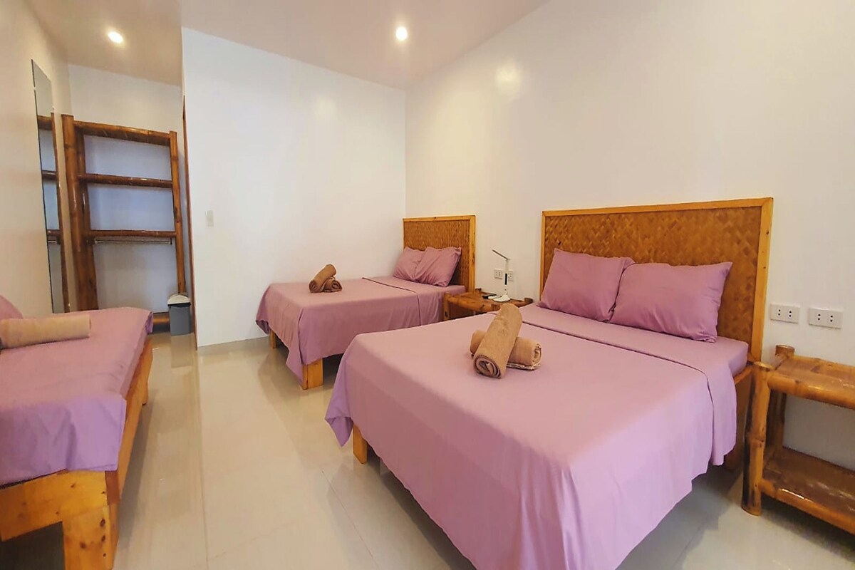 A hotel room with three beds, each with a wooden headboard and purple bedding.