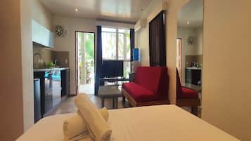 Quarto de hotel com uma cama, um sofá vermelho, uma TV e uma cozinha compacta.