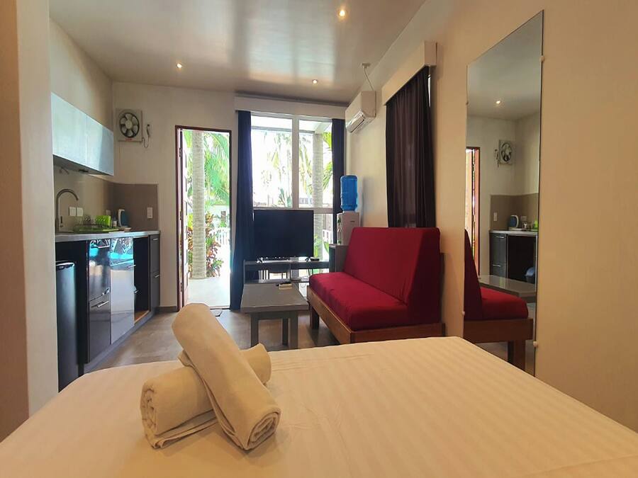 Quarto de hotel com uma cama, um sofá vermelho, uma TV e uma cozinha compacta.