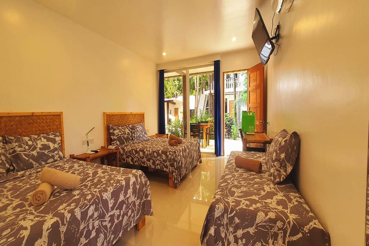 A hotel room with two beds, a TV mounted on the wall, and a view of the outside.