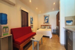 Ein Hotelzimmer mit einem roten Sofa, einem kleinen Tisch, einem Bett mit weißer Bettdecke, einem Wasserspender und einem Gemälde eines Hais an der Wand.