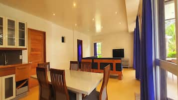 A spacious living area with a dining table, chairs, a TV, and a kitchen area with cabinets and a sink.