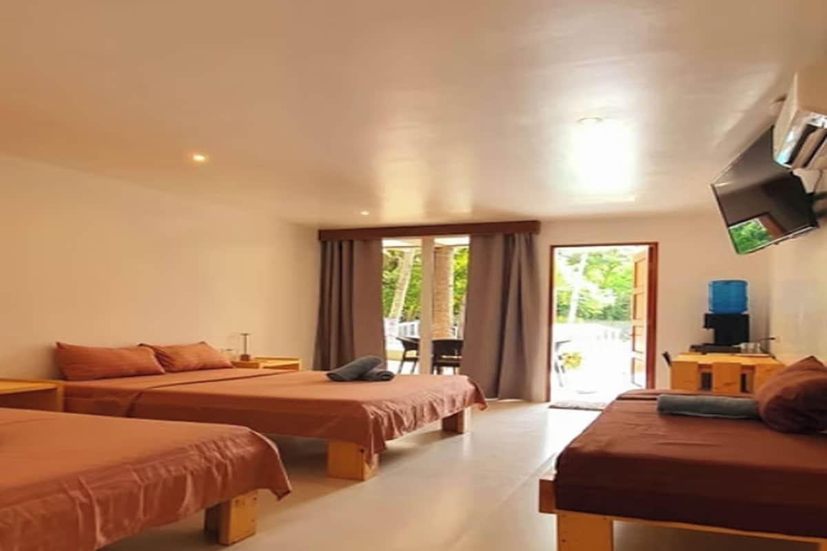 A hotel room with two beds, a flat-screen TV mounted on the wall, and a view of the outdoors through the window.