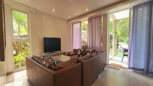 Uma sala de estar moderna com sofá seccional, televisão de tela plana e janelas amplas com vista para o exterior.