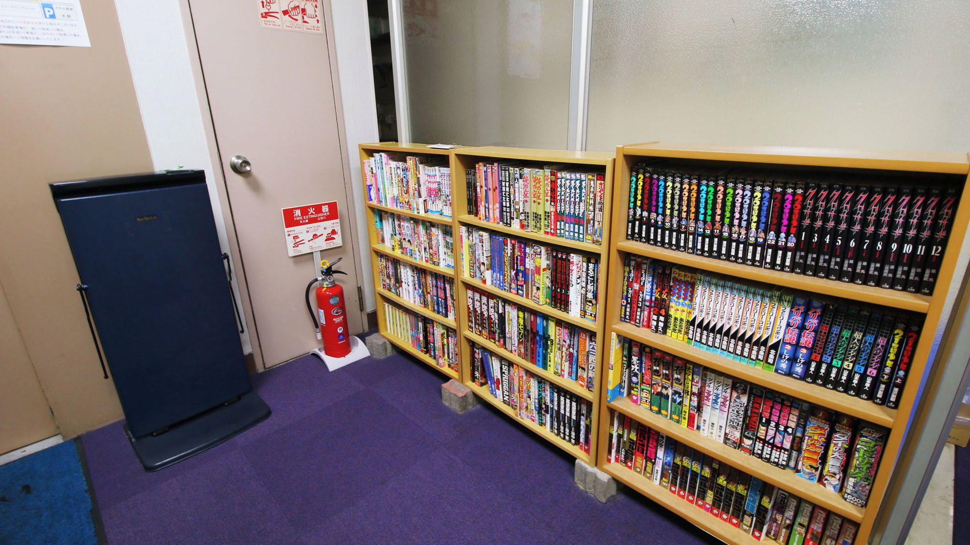 Una biblioteca con estanterías llenas de manga y un extintor en el suelo.