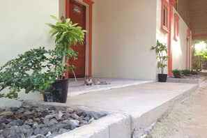 A building with a red door and windows, a cat lying on the porch, and potted plants. - Casa Paliton Siquijor Near Beach By Zuzu (San Juan)