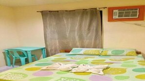 A single bed with a colorful polka dot bedspread, a small table, and a curtain. - Casa Paliton Siquijor Near Beach By Zuzu (San Juan)