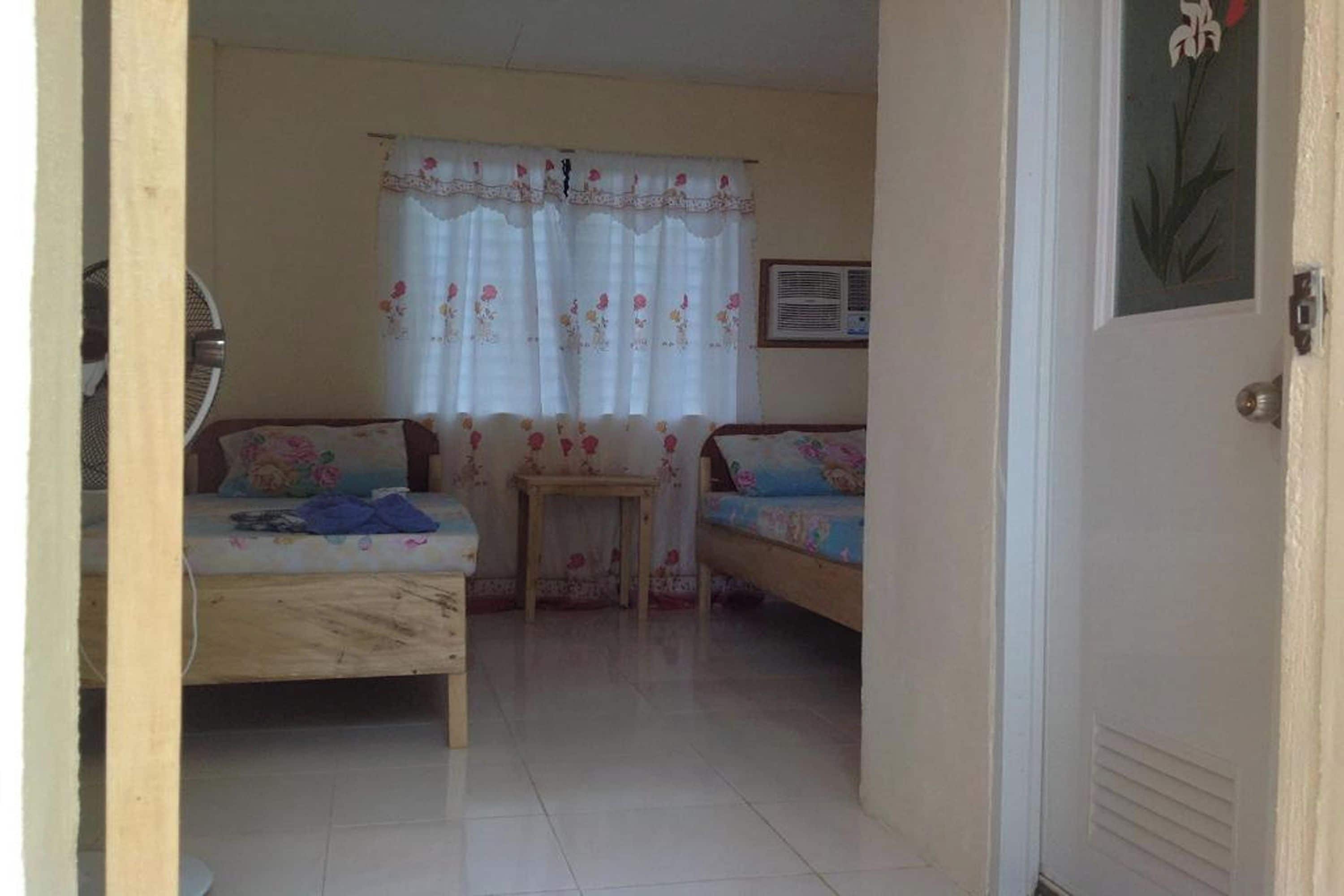 A room with two beds, a small table, and a window with floral curtains.