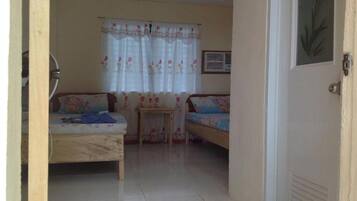 A room with two beds, a small table, and a window with floral curtains.