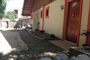 Un edificio con puerta roja y ventanas, un camino de grava y plantas en macetas.