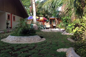 Un giardino tropicale con un edificio a tetto di paglia, sentieri in pietra e ombrelloni colorati.